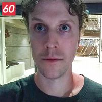 En person står i en ljus hall fylld med speglar och metalliska detaljer, med en nödutgångsskylt synlig i bakgrunden.