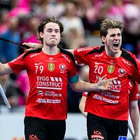 Två innebandyspelare i röda matchtröjor firar tillsammans på planen under en match.