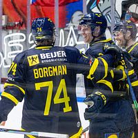 Tre ishockeyspelare firar ett mål framför sarg med reklamskyltar.