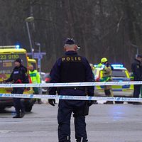 Polisavspärrning vid en väg med ambulanser och polisnärvaro i bakgrunden.
