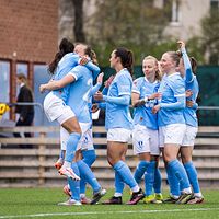 Damfotbollslag firar mål på gräsplan, spelare i ljusblå tröjor kramar varandra.