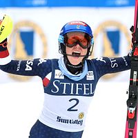 Alpin skidåkare med nummer två firar med uppsträckta armar, hållandes stavar och skidor.