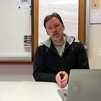 Person vid skrivbord framför laptop, i ett kontorsrum med whiteboard och anslag på väggen.