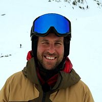 Person med skidkläder och hjälm på snötäckt fjäll.