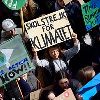 Greta Thunberg står i ett hav av demonstrater, hållandes ett plakat där det står ”Skolstrejk för klimatet”