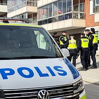 Polisbil och flera poliser utanför ett flerbostadshus.