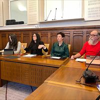 Möte i seminarierum; fyra personer vid skrivbord med laptopar och mikrofoner.