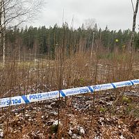 Ett avspärrningsband från polisen kring ett naturområde med buskar och träd