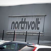 Northvolt-logga på fabriksbyggnad med bilar i förgrunden.