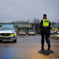 Polis stoppar trafik vid väg med polisbil och flera bilar i bakgrunden.