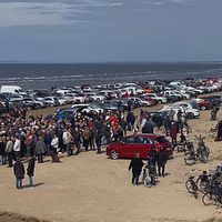 Tusentalsbilar och ännu fler människor står samlade på stranden, precis vid havet.