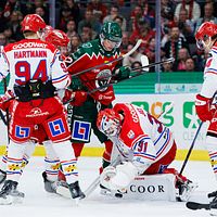 Hockeyspelare kämpar om pucken framför målvakten i en intensiv match.