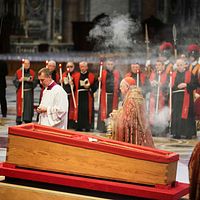 Kista omgiven av präster och vakter vid en ceremoni i en kyrka.