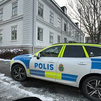 Polisbil parkerad utanför en herrgårdslik byggnad på en snötäckt gata.