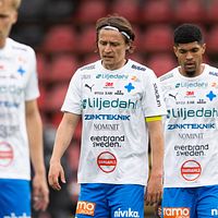 Tre fotbollsspelare i vita matchställ på planen.