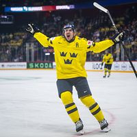 Svensk ishockeyspelare jublar efter mål under match, publik syns i bakgrunden.