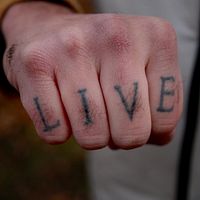 Hand med tatuering där det står ”live”