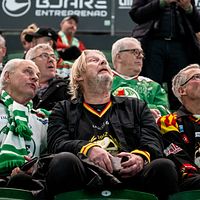 Rolf Lassgård och flera andra Brynässupportrar i klubbtröjor sitter på läktaren under en match.