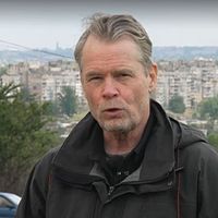 Person utomhus med stad och parkerade bilar i bakgrunden.