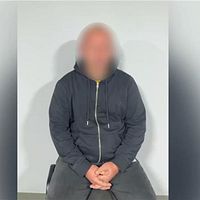En man med blurrat ansikte sitter på en stol med knäppta händer framför en vit vägg. Bilden kommer från Ukrainska SBU via Telegram.
