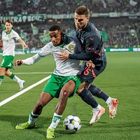 Två fotbollsspelare kämpar om bollen nära sidlinjen på en upplyst arena.