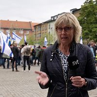 SVT:s reporter på ett torg. Bakom står personer som viftar med israeliska flaggor.