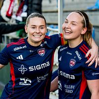 Två fotbollsspelare i blå matchställ firar tillsammans på en fotbollsarena.