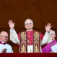 Påve står på en balkong med händerna upplyfta, flankerad av präster i liturgiska kläder.