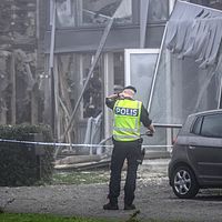 En polis med ryggen vänd mot fotografen står framför ett förstört hus.