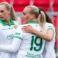 Fotbollsspelare i gröna shorts firar på planen. Röda stolar syns i bakgrunden.