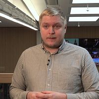 En person med randig skjorta står inomhus framför en träpanel och stora lampor.