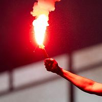 Supportersvimmel på läktare, en person håller upp en röd bengal.