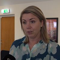 På bilden syns en blond kvinna med halvlångt blont hår och en blå blommig blus.