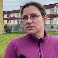 Person i lila tröja intervjuas utomhus framför en byggnad.