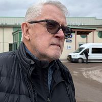 En person i en svart jacka står framför en byggnad med en vit minibuss i bakgrunden.