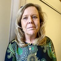 Kvinna i mönstrad klänning i kontorsmiljö, grön klädhängare i bakgrunden.