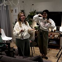 Tre kvinnor spelar in video i ett vardagsrum, omgiven av kamera och belysning.