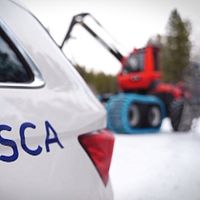 SCA-logotyp på bil med en skogsmaskin i bakgrunden på en snötäckt väg i skogarna kring Backe, i Strömsunds kommun.