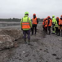 Grupp personer i varselkläder står vid grusig kant nära ett stenbrott eller gruva.