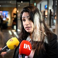 Person intervjuas av flera reportrar med mikrofoner från SVT och DN i en offentlig miljö.