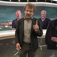 Person gestikulerar framför täckta ansikten på en tv-studio.