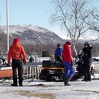 Flera personer är på väg att sätta sig i skoter och pulka för en av säsongens sista turer i Nikkaluokta.