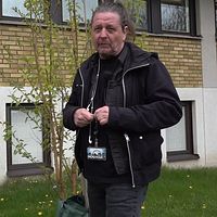 Person med ID-bricka står utomhus framför en byggnad med gula tegelväggar och fönster.