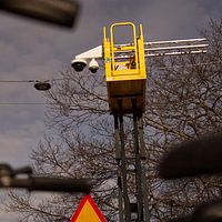En gul kran med kamera är uppställt nära träd med cykelstyre synligt i förgrunden.