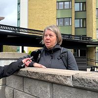 Reporter intervjuar en person vid en mur utanför ett flerbostadshus.