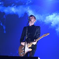Musiker med gitarr på scen under blått ljus.
