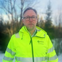 Jonas Mårtensson från SCA står med varseljacka, glasögon framför en skog i en snöigt landskap, utanför Östersund.