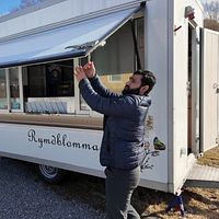 Saed Atiqullah öppnar luckan på en matvagn utomhus. Soligt väder och blå himmel.
