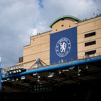 Chelsea FC:s klubbmärke syns på en byggnad vid Stamford Bridge under molnig himmel.