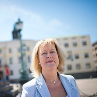Kvinna i ljus kavaj på Göteborgs Gustav Adolfs torg med statyn i bakgrunden.